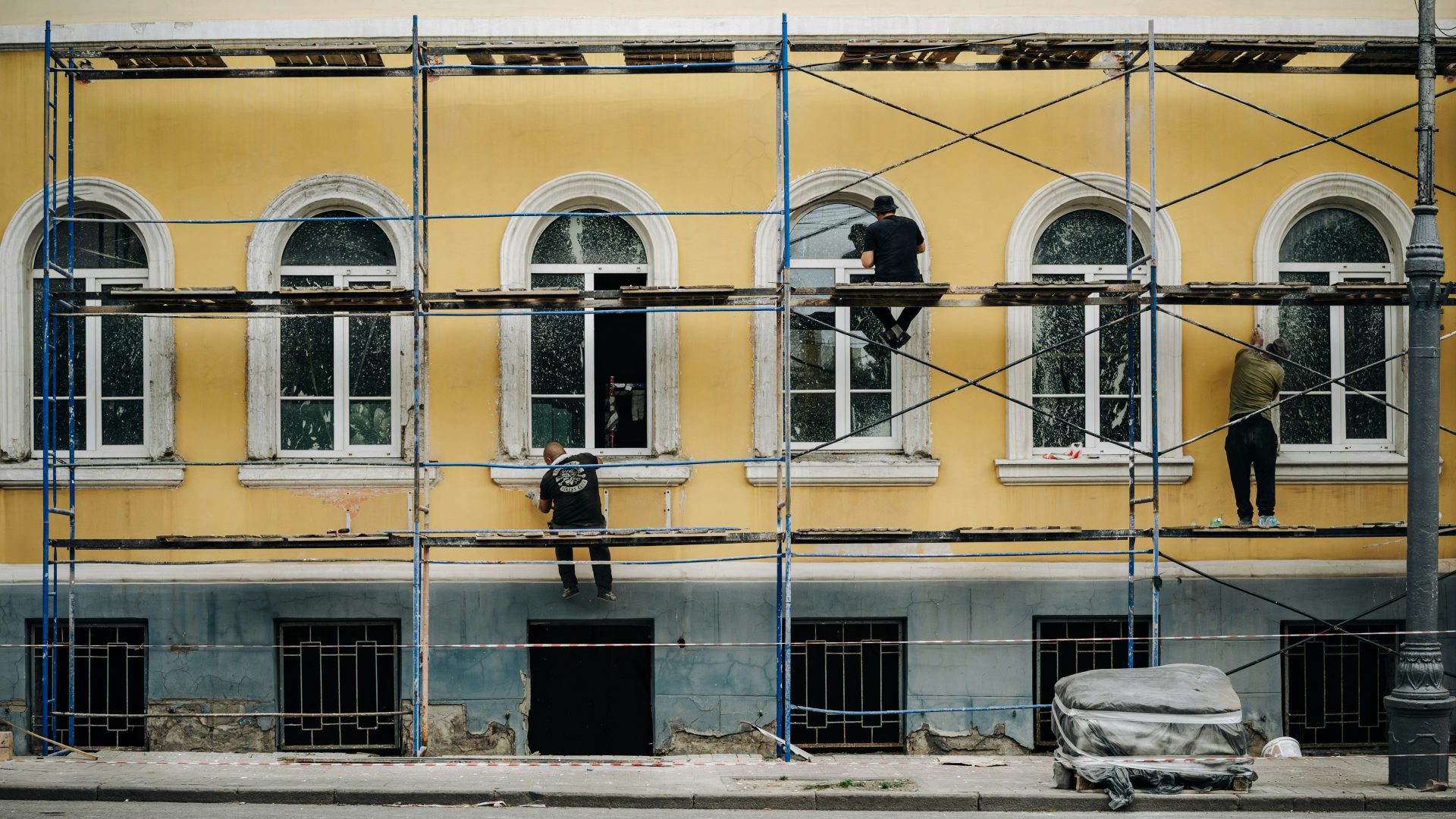 Workers on scaffolding repairing a yellow building facade.
